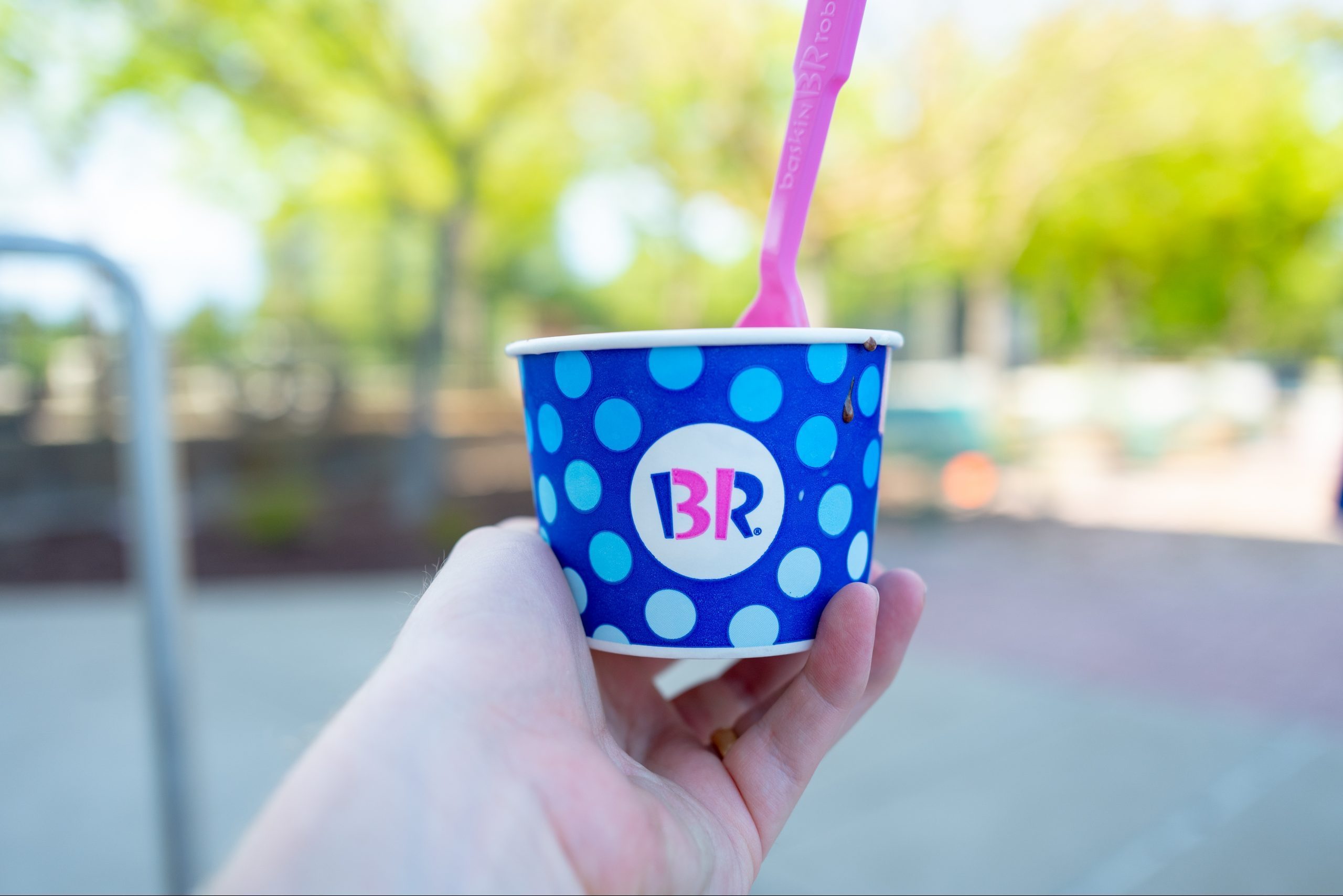 hand holding out a cup of baskin robbins ice cream outdoors on a sunny day