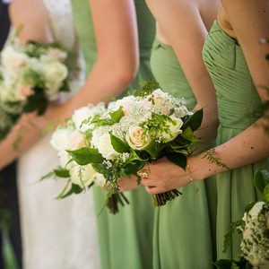 A candid photo of bride and her bridesmaids wearing light green bridesmaid dresses and holding a gorgeous bouquet. White and pink roses with baby's breath and green accents