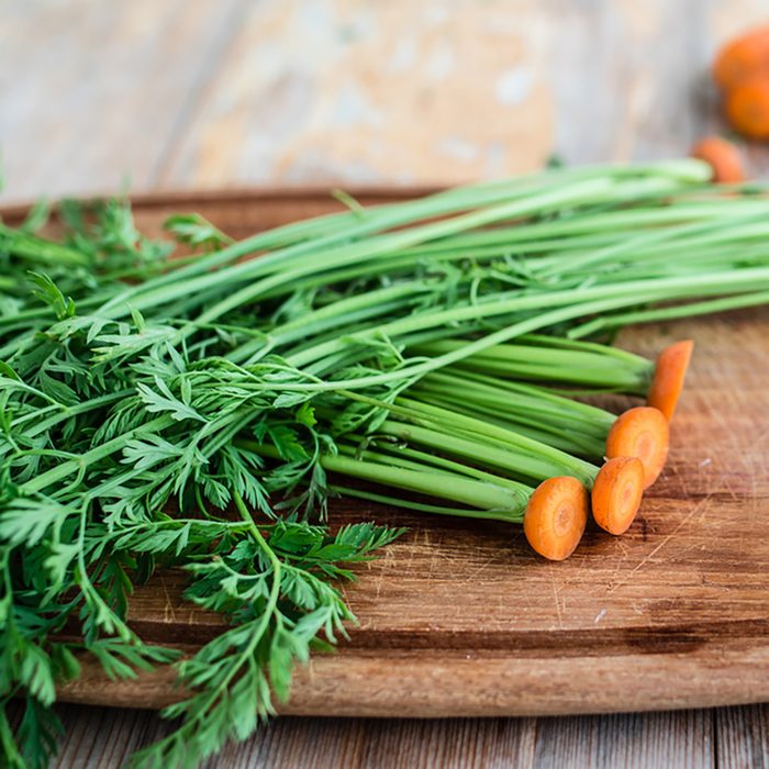 Green tops of carrots on wooden board.