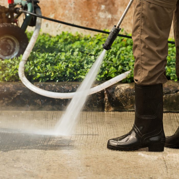 Worker cleaning driveway with gasoline high pressure washer splashing the dirt