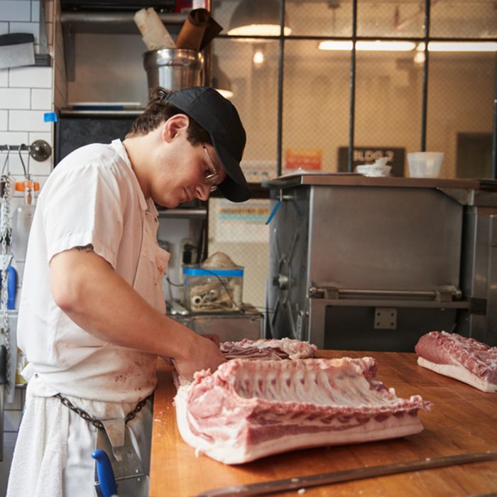 Young butcher cutting meat to sell at a butcher's shop