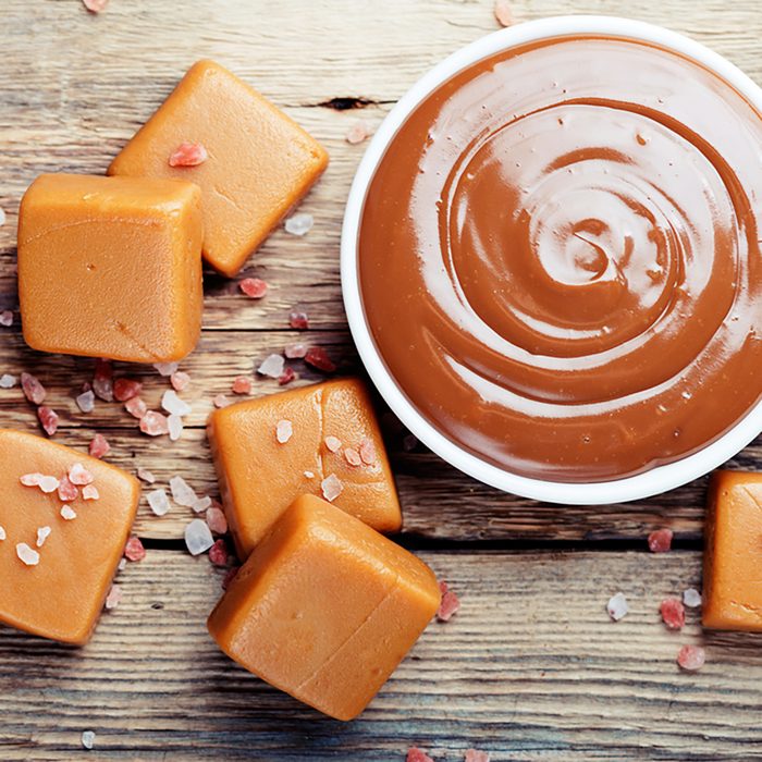 Melted caramel with pieces of caramel candy with salt on a wooden table.