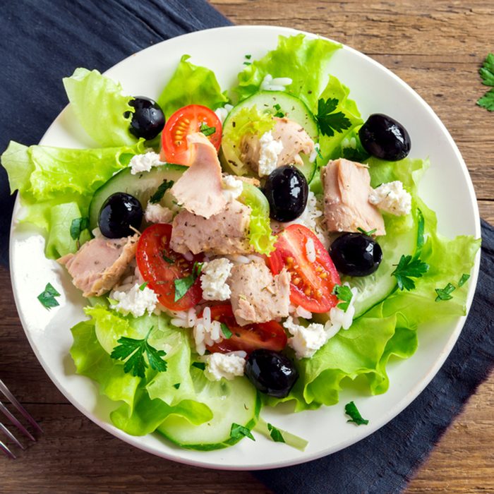 Tuna salad with tomatoes, black olives, rice, feta cheesse and greens on rustic wooden background with copy space