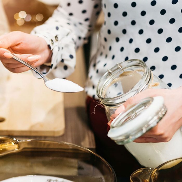Woman cafe worker adding sugar to bowl with dessert ingredients.
