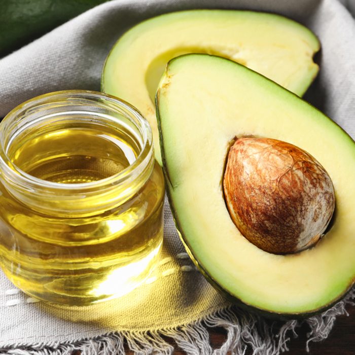 Jar with oil and ripe fresh avocado on table