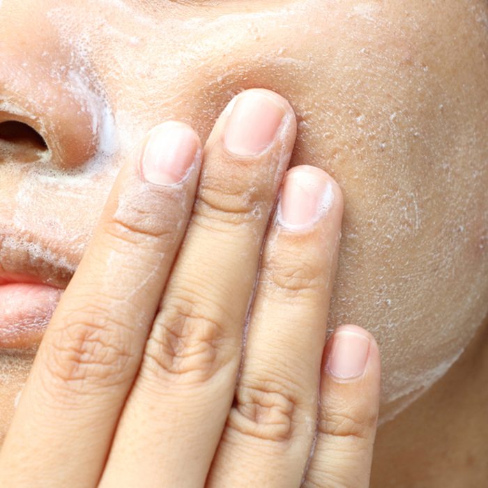 Woman washing face (have wide pores) with white foam by her hand.