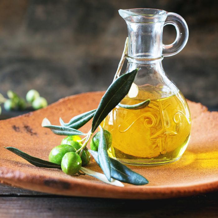 Bottle of olive oil with olive branch in handmade clay plate over wooden table.