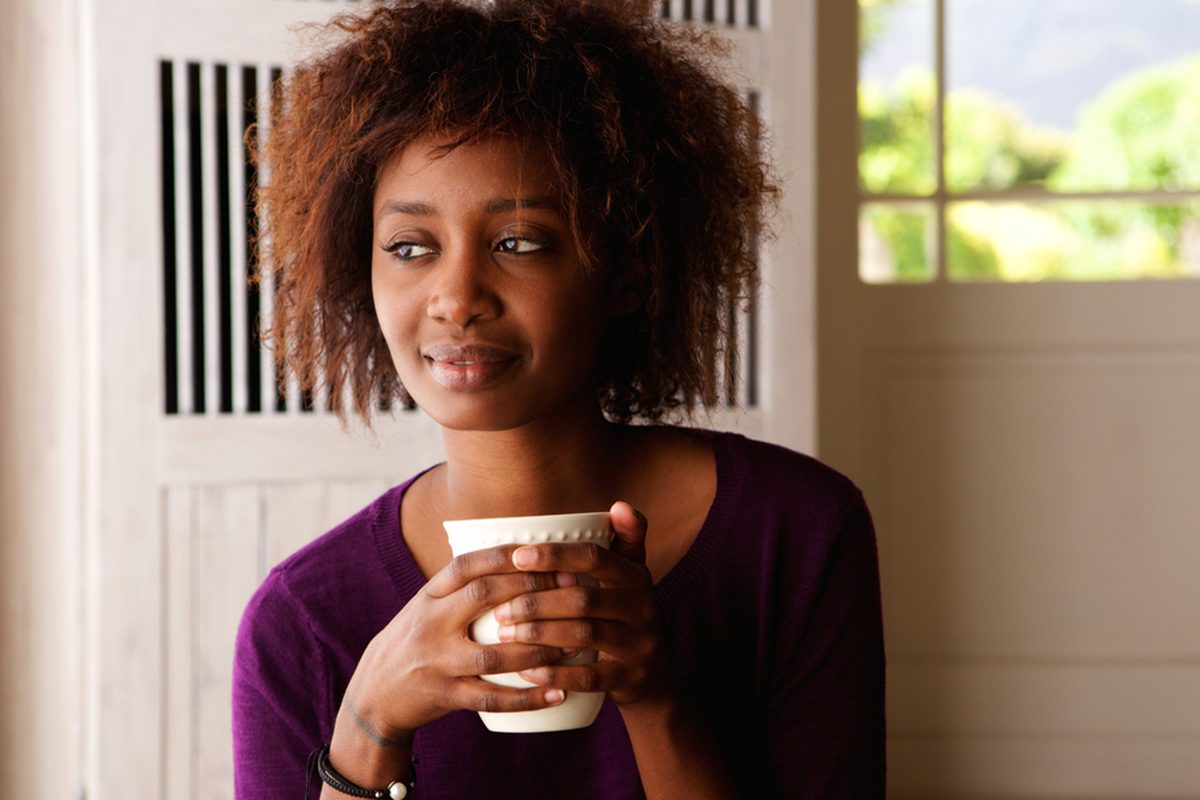 Close up portrait of a beautiful young african american woman enjoying cup of coffee at home