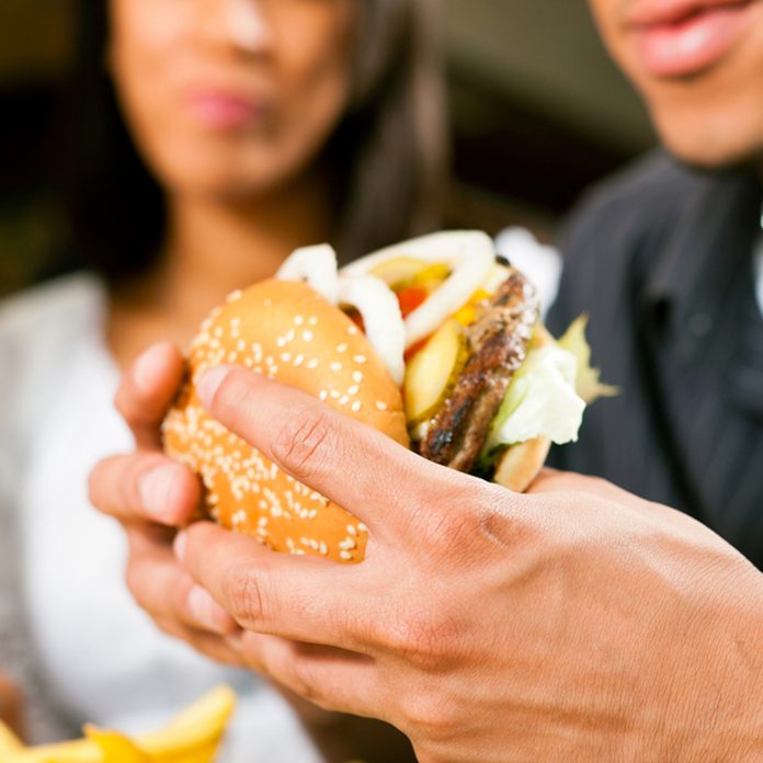 Happy man (African American) in a fast food restaurant eating a hamburger with his girlfriend