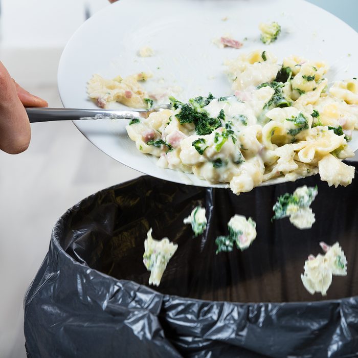 Close-up Of A Person Throwing The Leftover Pasta Into The Trash Bin