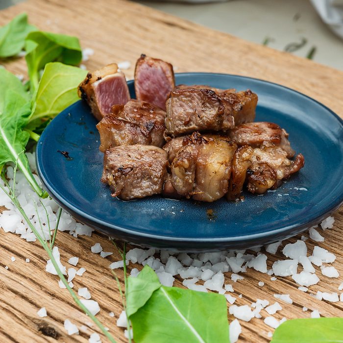 Medium Rare Fried Diced Marinated Beef on Blue Ceramic Plate on Wood Panel with Sea Salt and Vegetable Decorated.