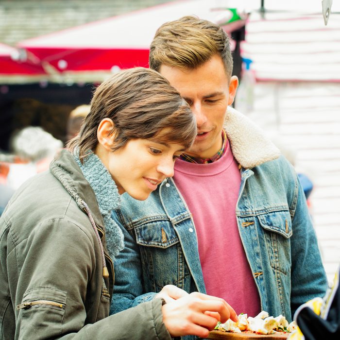 Young British couple sampling food at London market. They are dressed in Autumn clothing and the female is pickeing up chicken pieces to taste.