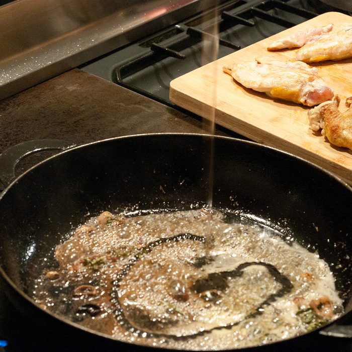 motion blur of deglaze, floating liquid into gravy in an hot iron pan on range, fried chicken pieces in backround on wooden cutting board