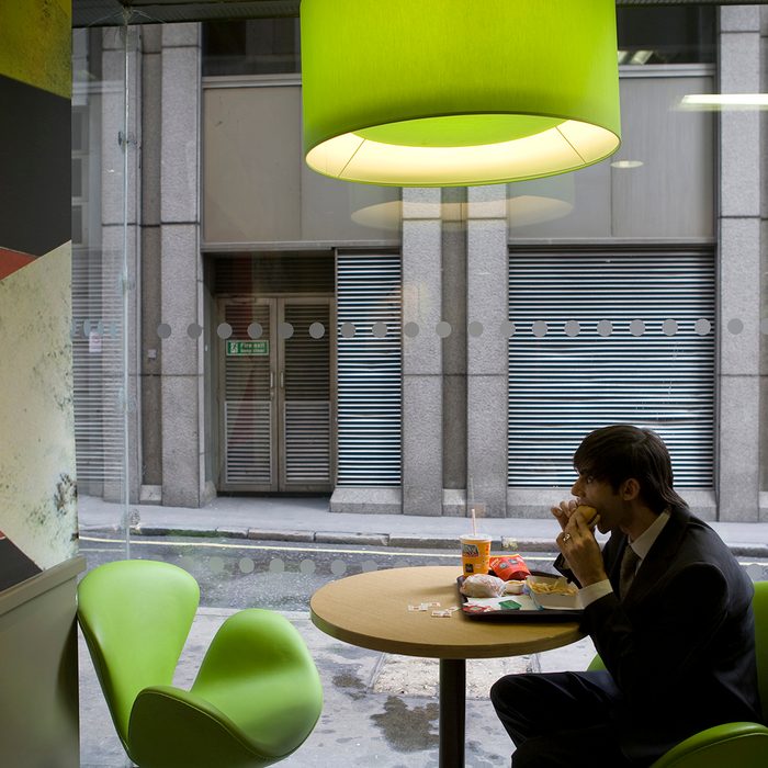A McDonald's customer tucks into his Big Mac, oblivious to the new trendy coffee bar style ambience and design at the Cannon Street branch of McDonalds in the City of London. This is one of the flagship branches for this new design as the corporation takes on the process of 're-imaging' the fast food chain. This redesign, with new colours: khaki, lime, orange and russet, in a vibrant mixture of geometrics, lines and swooshes has been created for McDonald's by French Designer, Philippe Avanzi. It includes comfortable easy-chairs and stools, drop down lighting and in total, a whole new feel. This is part of a new global strategy to give McDonalds branches in different countries a uniquely local character, both in terms of the decor and some of the food served. The menu has even seen the introduction of sustainably grown coffee, organic milk etc. (Photo by Gideon Mendel/Corbis via Getty Images)