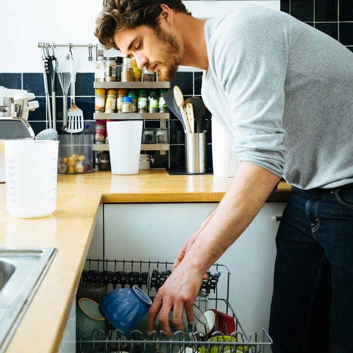 Man at home loading the dishwasher, putting dirty dishes into the machine.