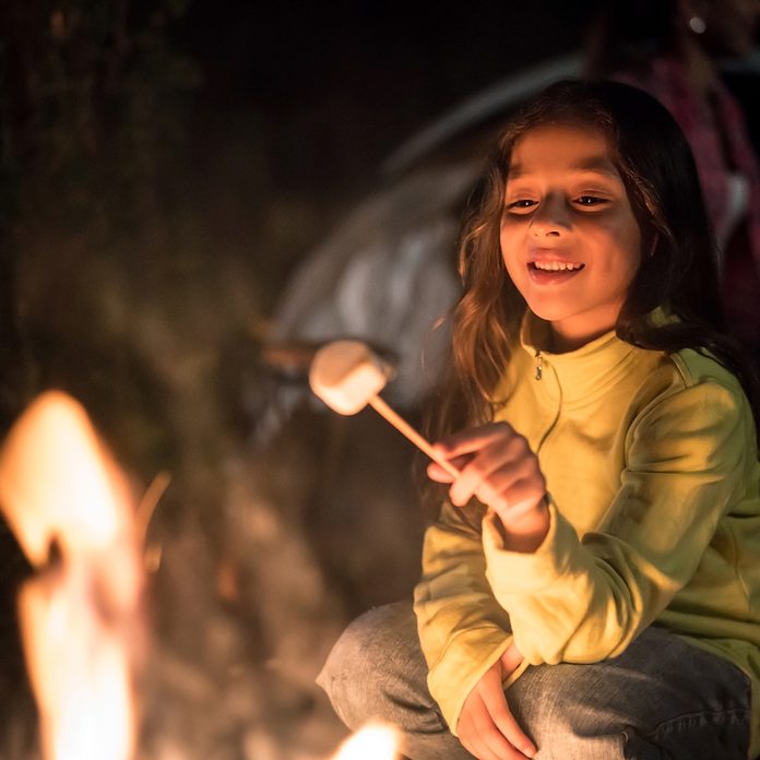 easter egg hunt ideas Portrait of a happy girl sitting outdoors by a bonfire eating marshmallows – outdoors lifestyle concepts