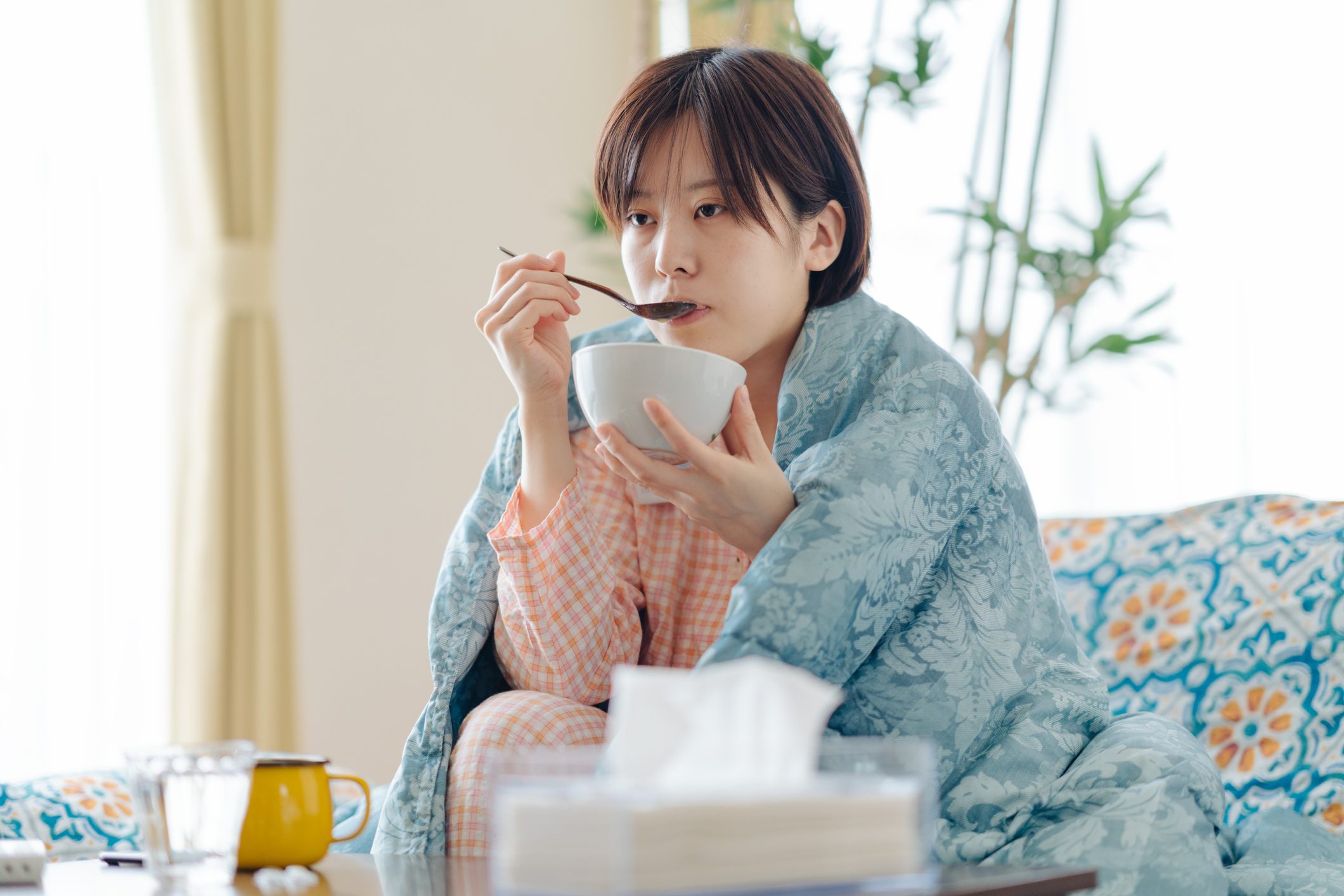 Sick Woman wrapped in a blanket eating soup on the couch