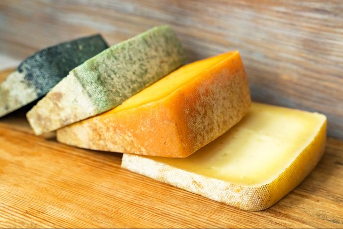 Different colors of craft cheeses assortment on natural wooden board. Cheese board concept