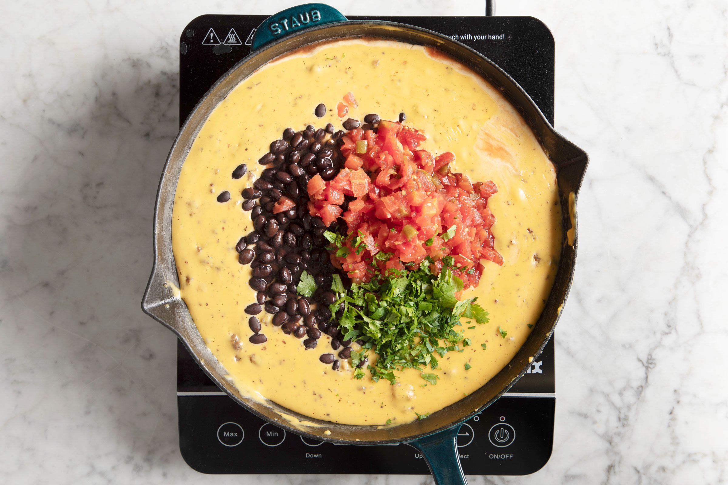 adding in beans, tomatoes and cilantro into the melted cheese with beef