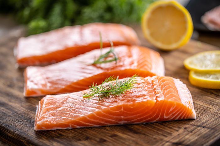 Raw salmon fillets onwooden cutting board with dill, rosemary and lemon.