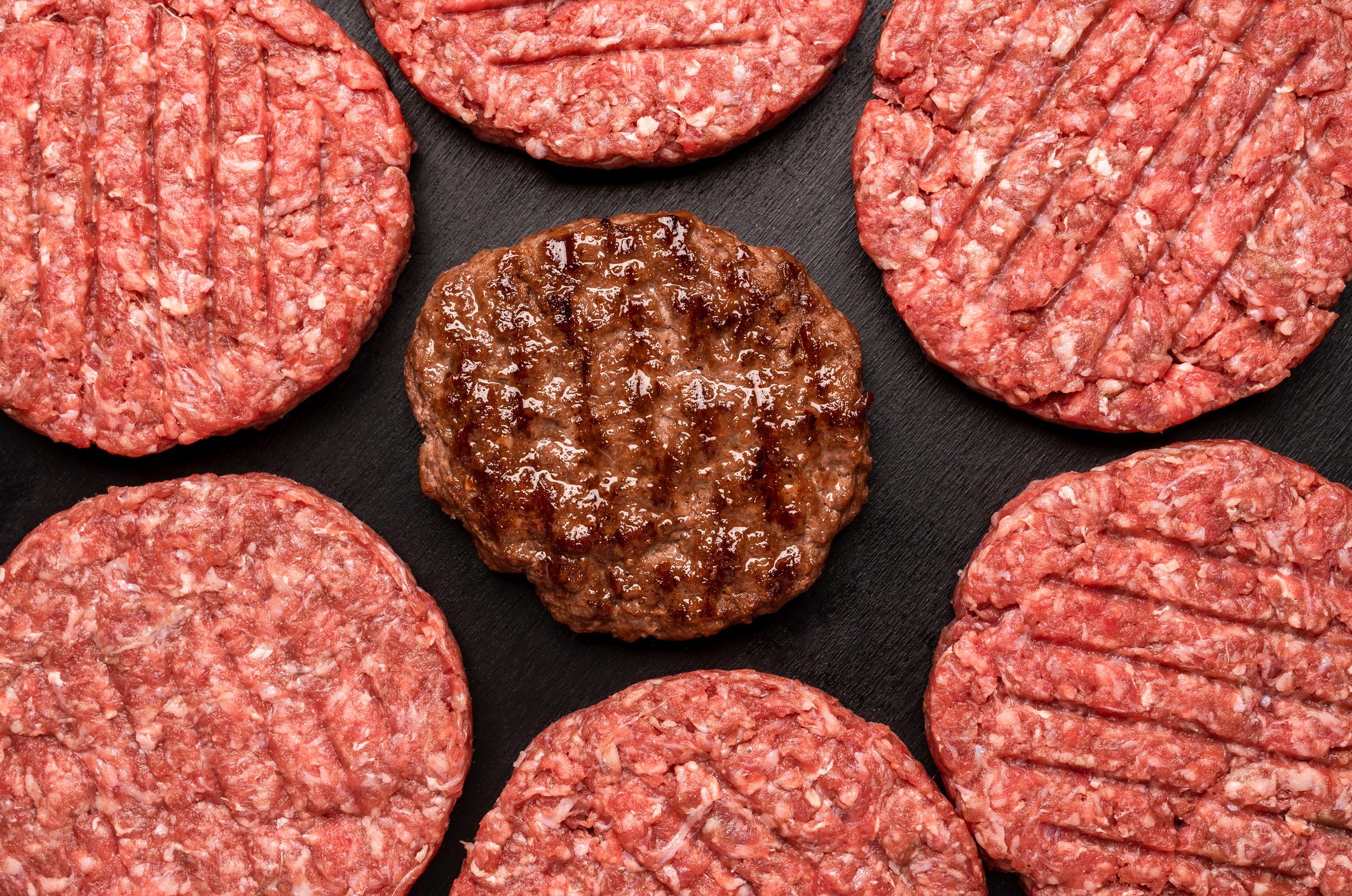 Raw and Grilled Hamburger patties top view on black table