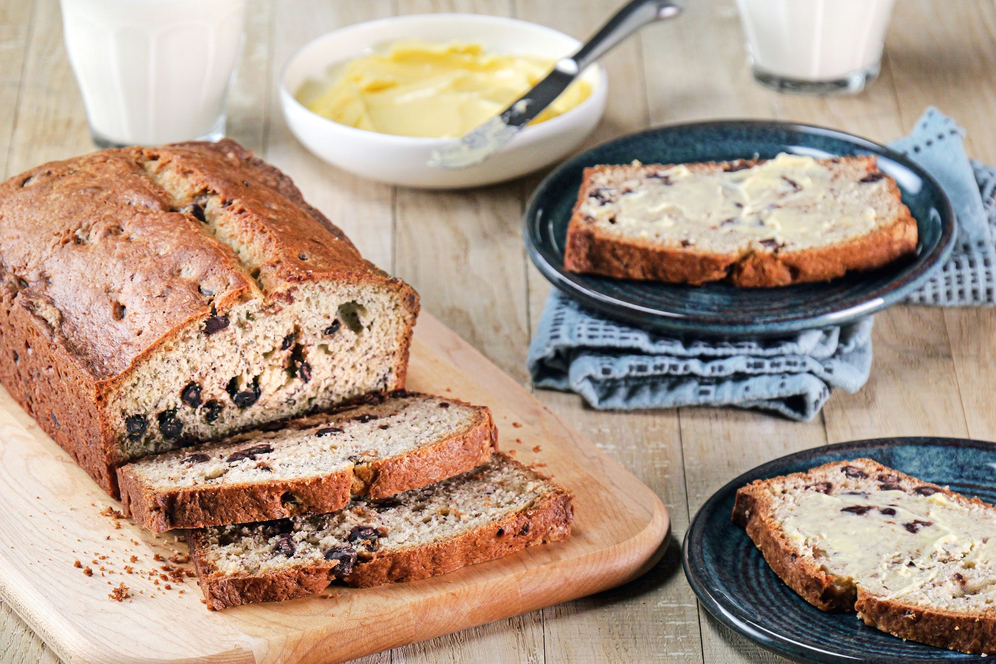 Chocolate chip banana bread on a wooden chopping board and chocolate chip banana bread on a small plate next to it
