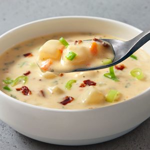 3/4th close shot; horizontal; light grey background; Potato Soup in small white bowl; a close view of Potato Soup in spoon;