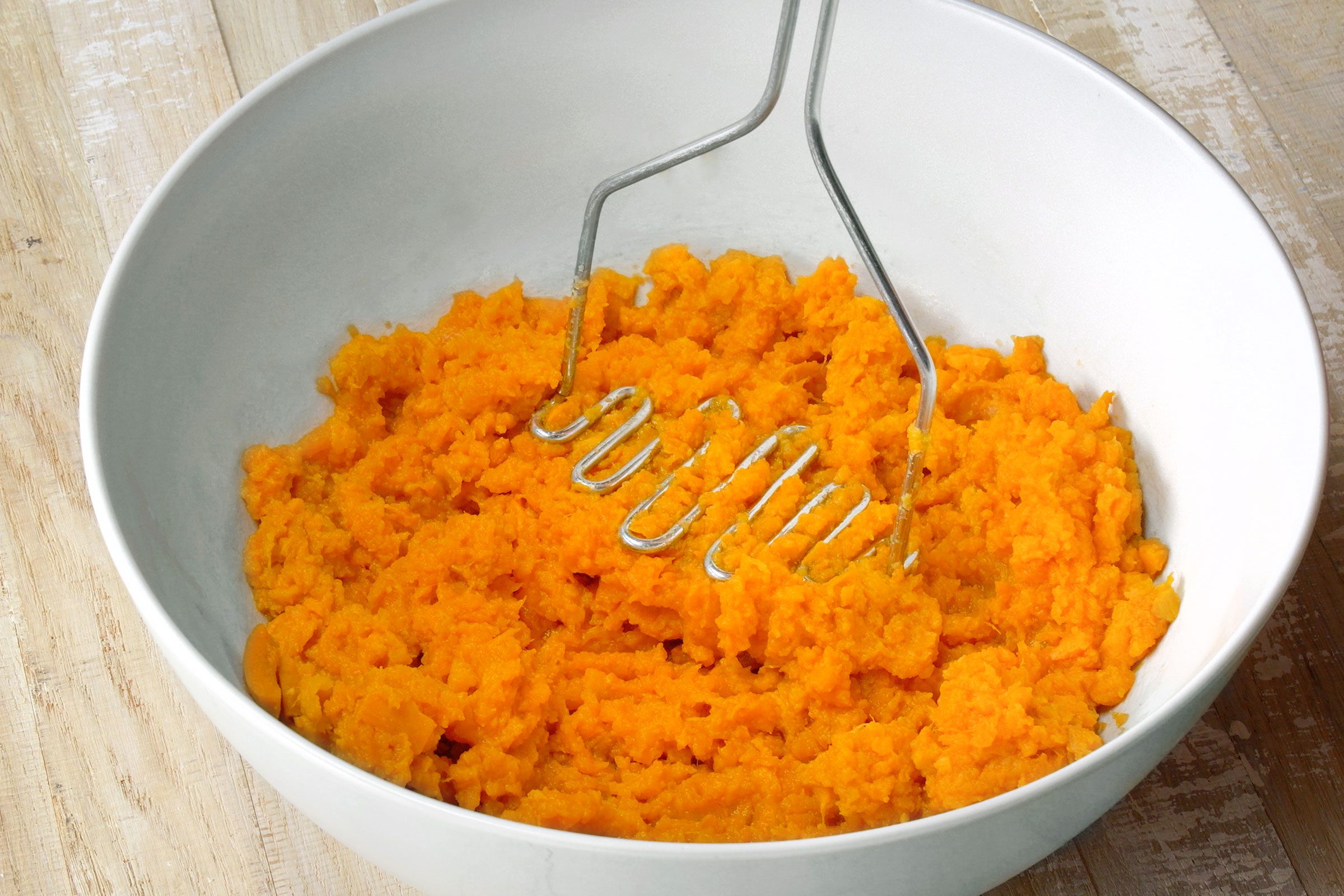 Mushing the boiled sweet potato pieces in a large white bowl
