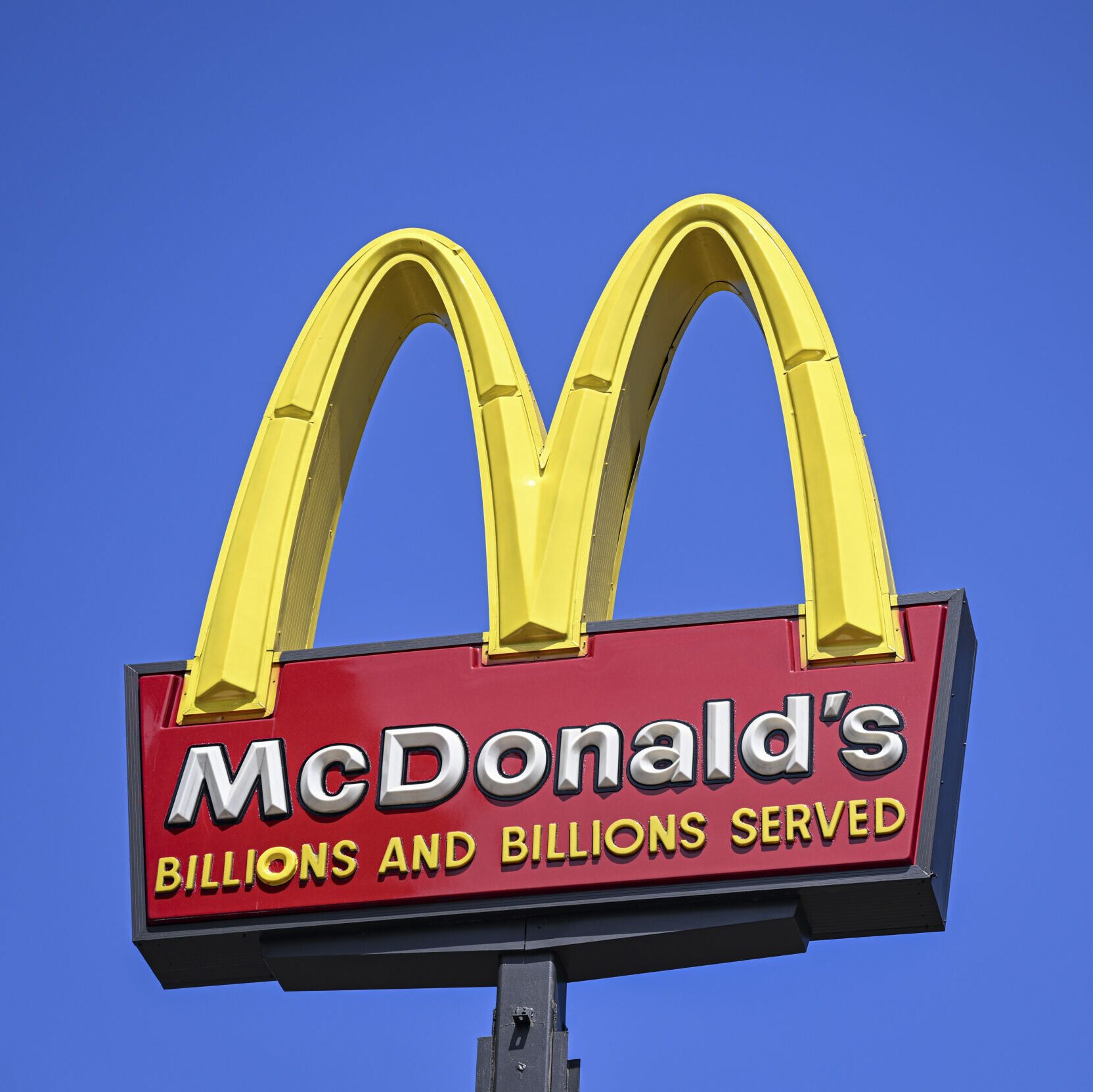 McDonald's sign with the golden arches and a "Billions and billions served" slogan on a red slab, with a blue sky background