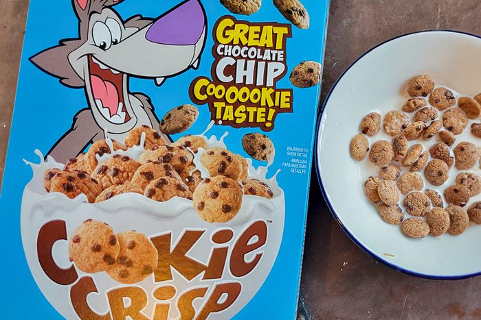 Box of Cookie Crisp cereal with a cartoon wolf and a bowl filled with chocolate chip cookie-shaped cereal and milk. The box features the text "Great Chocolate Chip Cooookie Taste!.