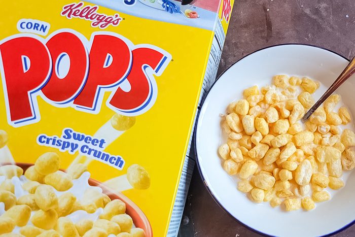 A box of Kellogg's Corn Pops cereal with "Sweet Crispy Crunch" written on it is next to a bowl filled with the cereal and milk. A spoon is in the bowl, ready for eating.