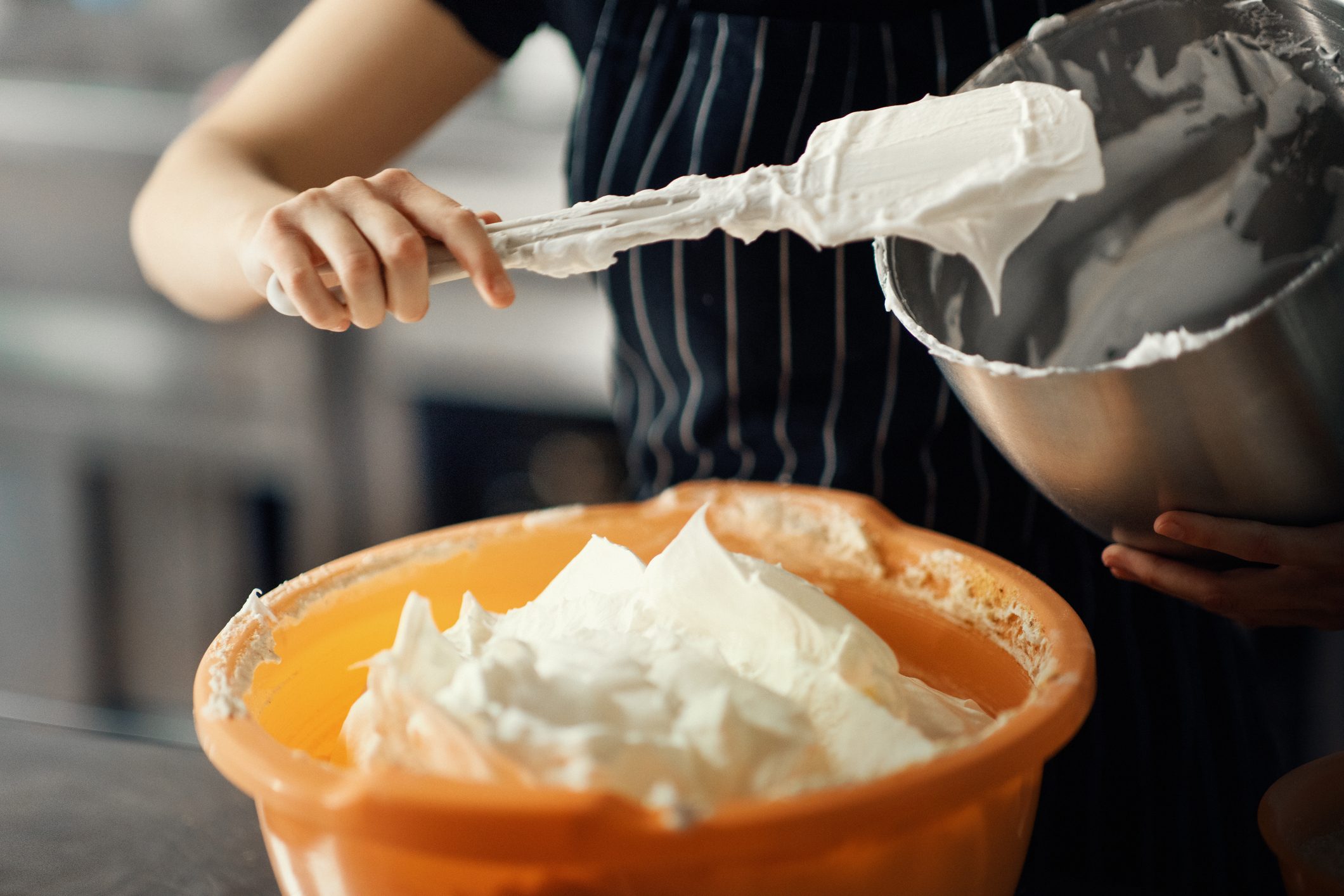 Baker transfers buttercream frosting into an orange bowl with a spatula
