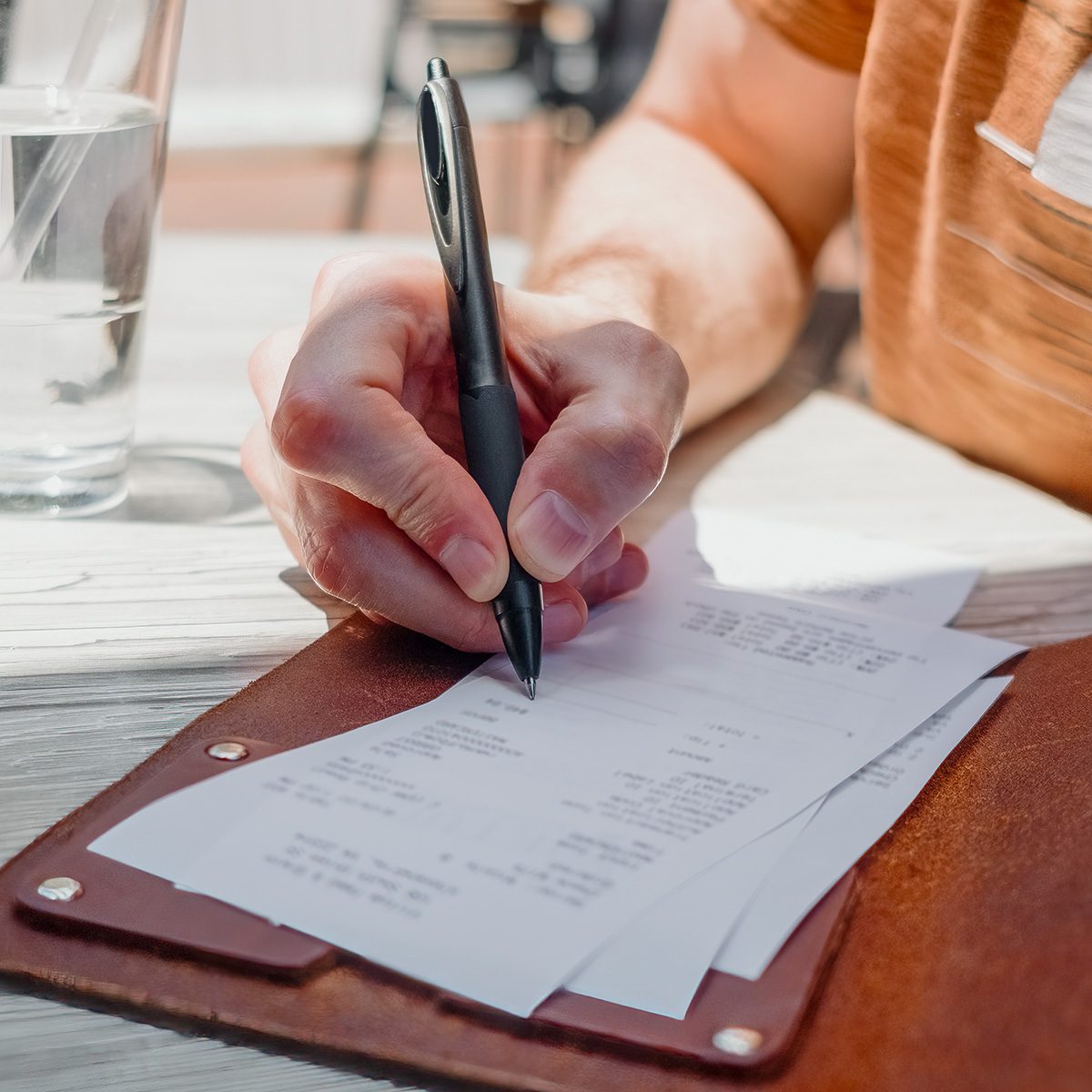 Close-up of unrecognizable white man writing in tip amount on credit card receipt at restaurant