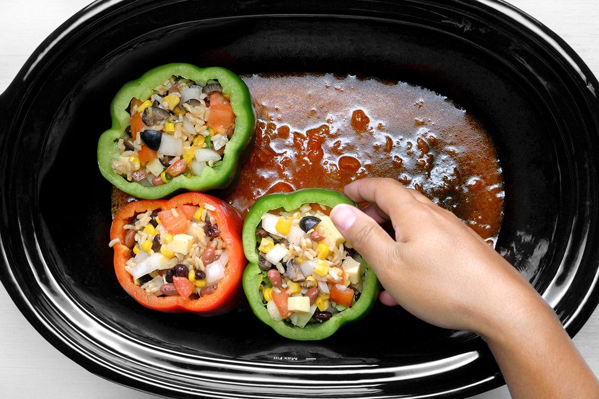 overhead shot of a slow cooker filled with stuffed bell peppers, The peppers are red and green, and they are filled with a mixture of rice, vegetables
